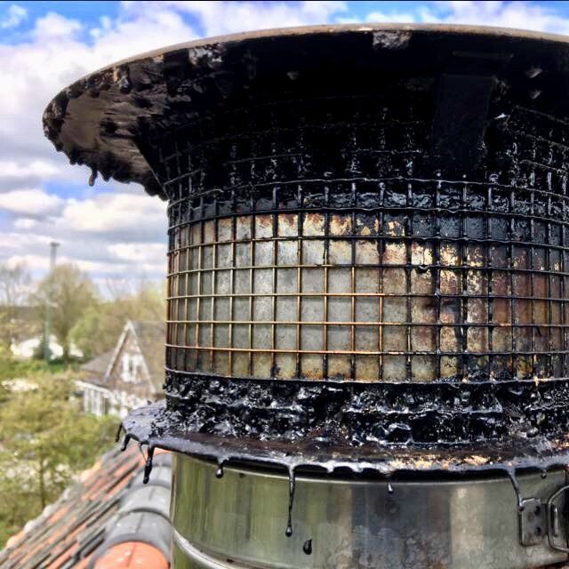 Een close-up van een metalen schoorsteenkap die zwaar bedekt is met een dikke, zwarte, teerachtige creosootlaag en daarvan druipt.
PEVAHO Helmond