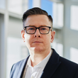 A man wearing glasses and a suit is looking at the camera.