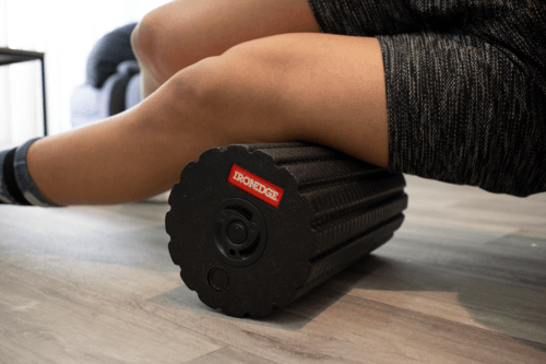 A woman is laying on the floor with a foam roller on her leg.