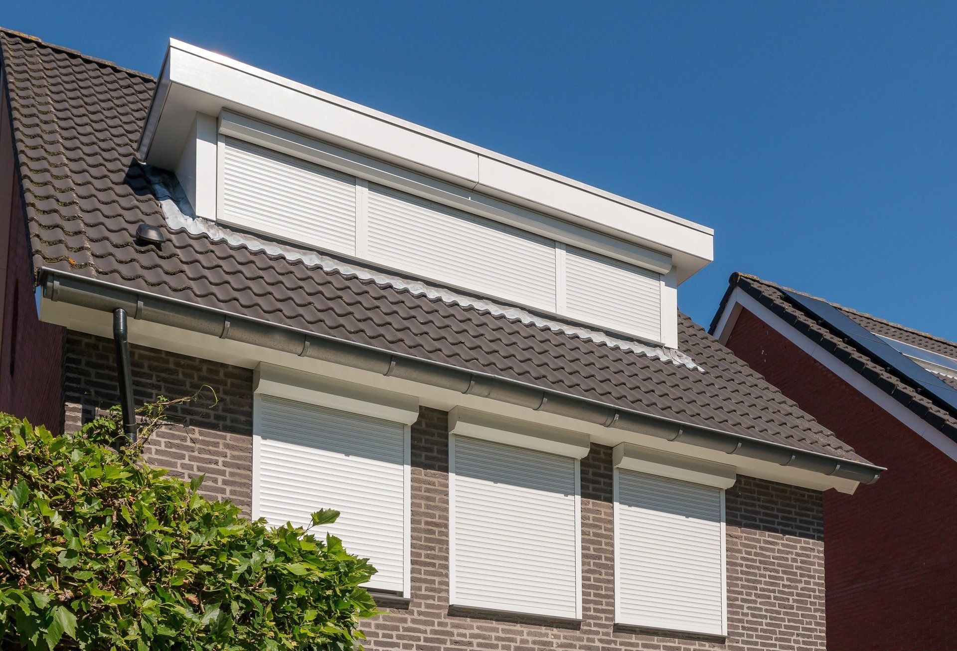 Een huis met een bruin dak en witte luiken voor de ramen