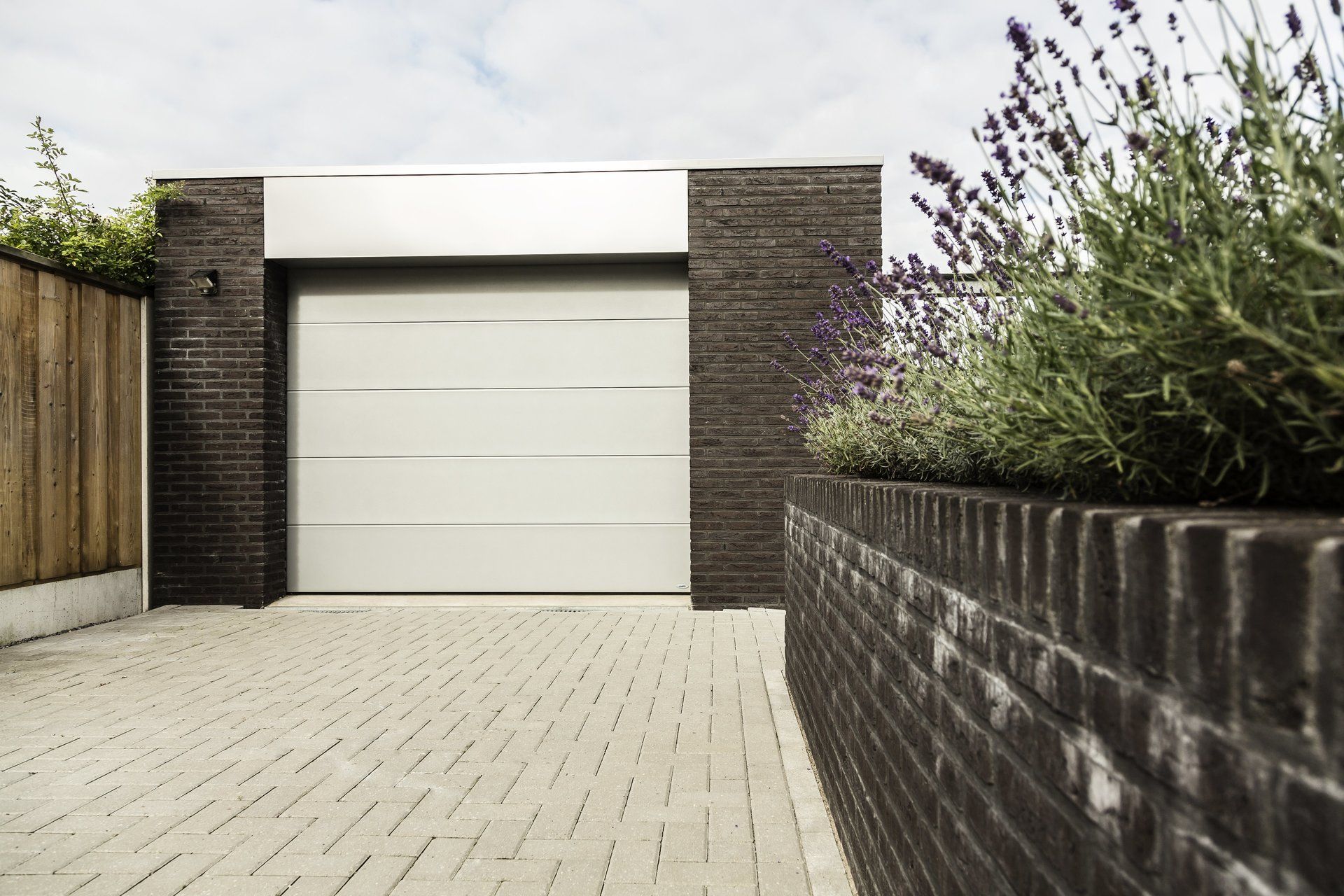 Een witte garagedeur staat naast een bakstenen muur.