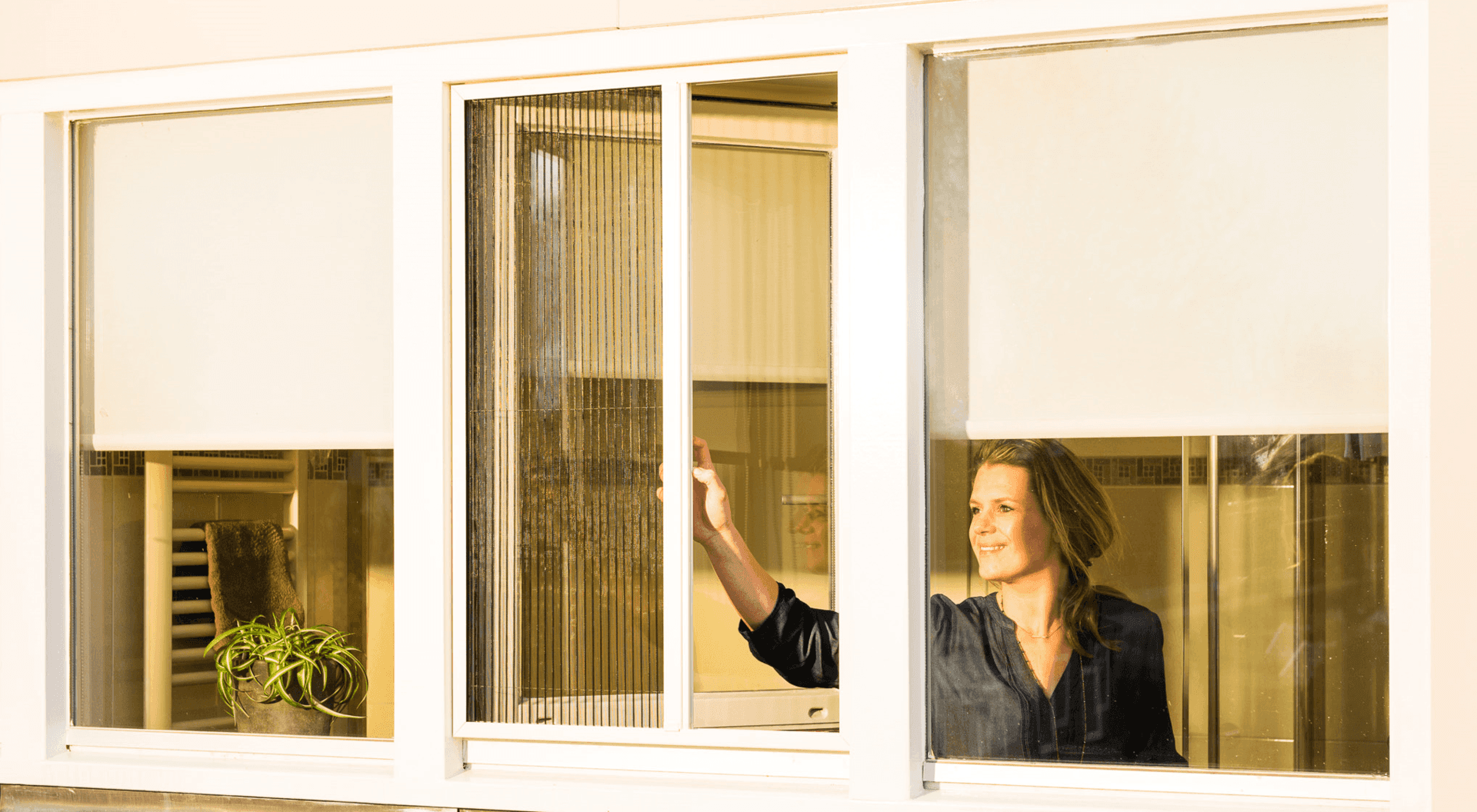 Een vrouw kijkt uit een raam waar jaloezieën voor hangen.