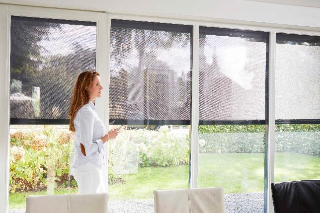 Een vrouw staat voor een groot raam in een woonkamer.