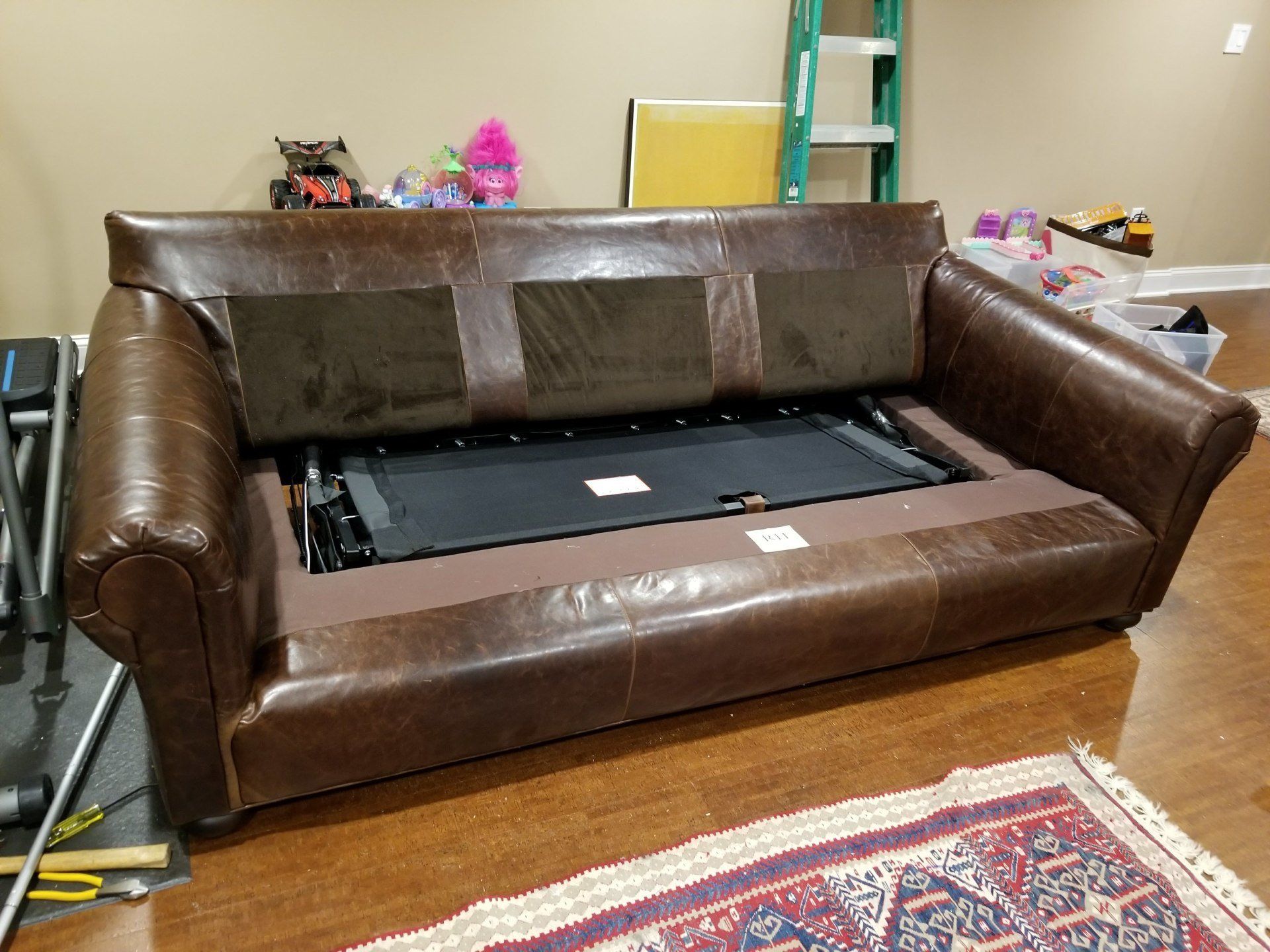Brown leather sofa bed with the back partially opened, revealing the inner mechanism.
