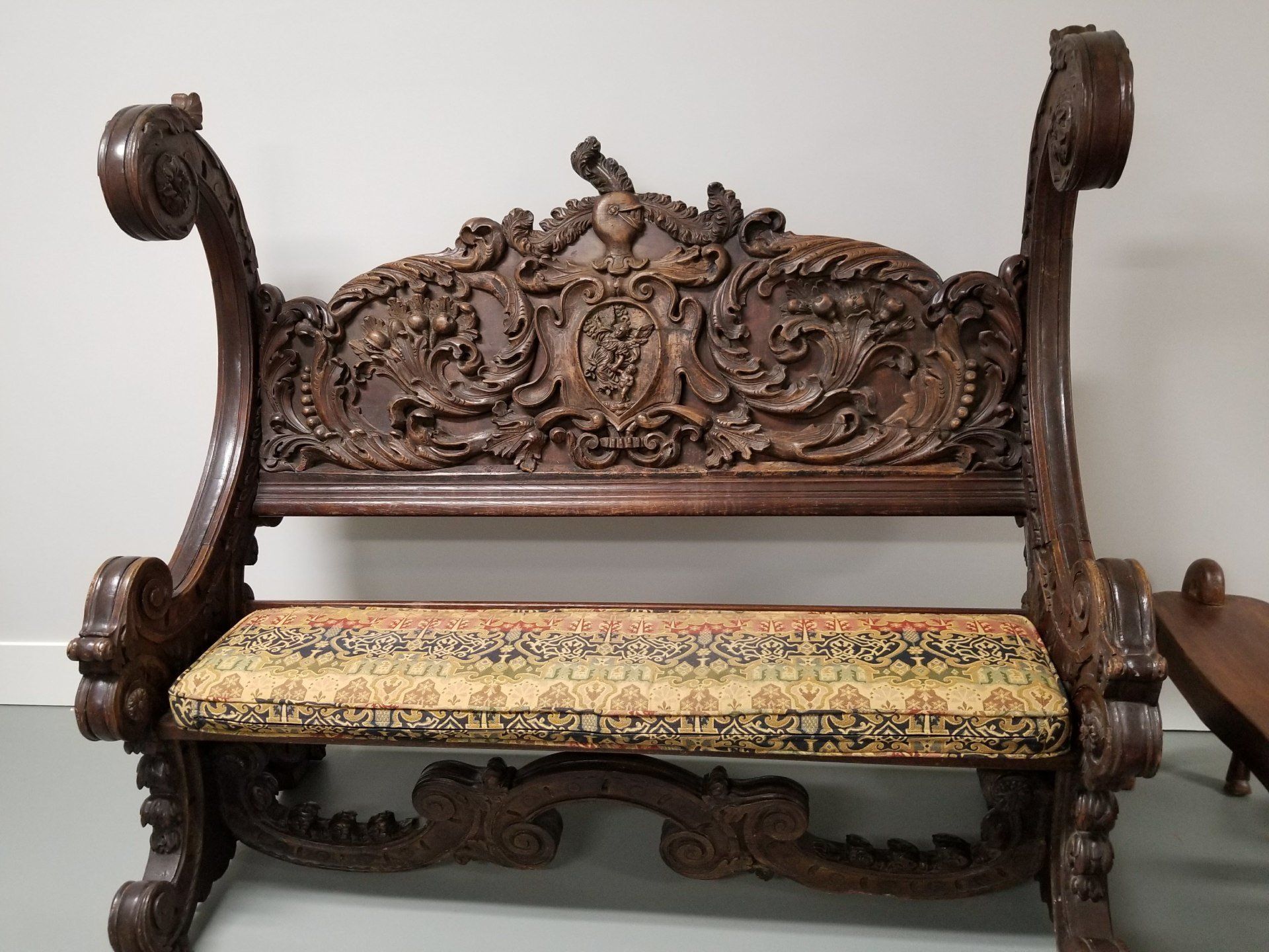 Ornately carved wooden bench with upholstered seat.