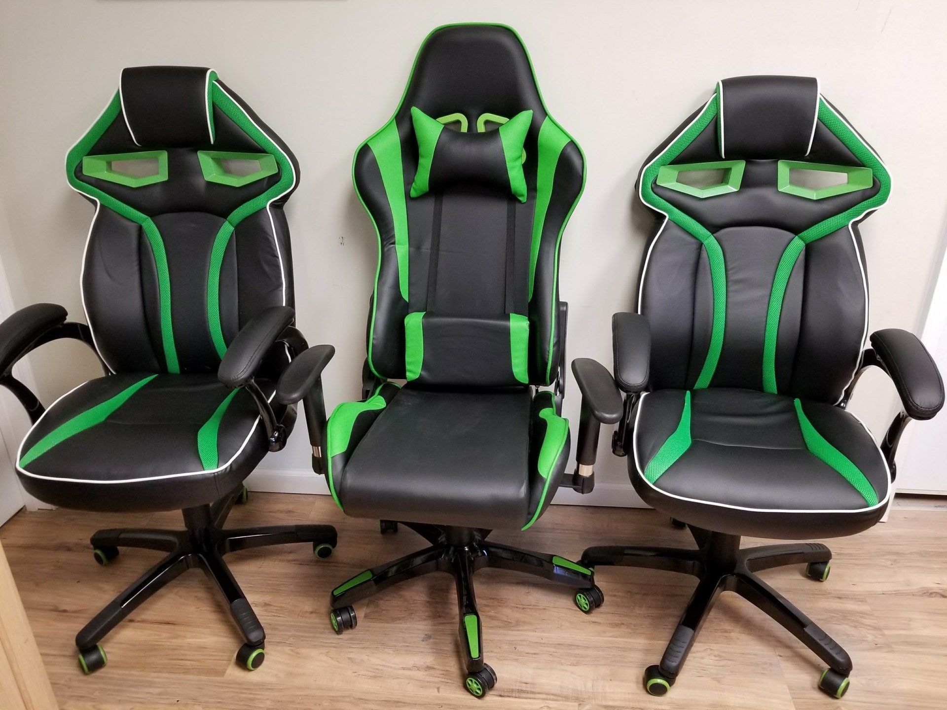 Three black and green gaming chairs are lined up on a wooden floor.