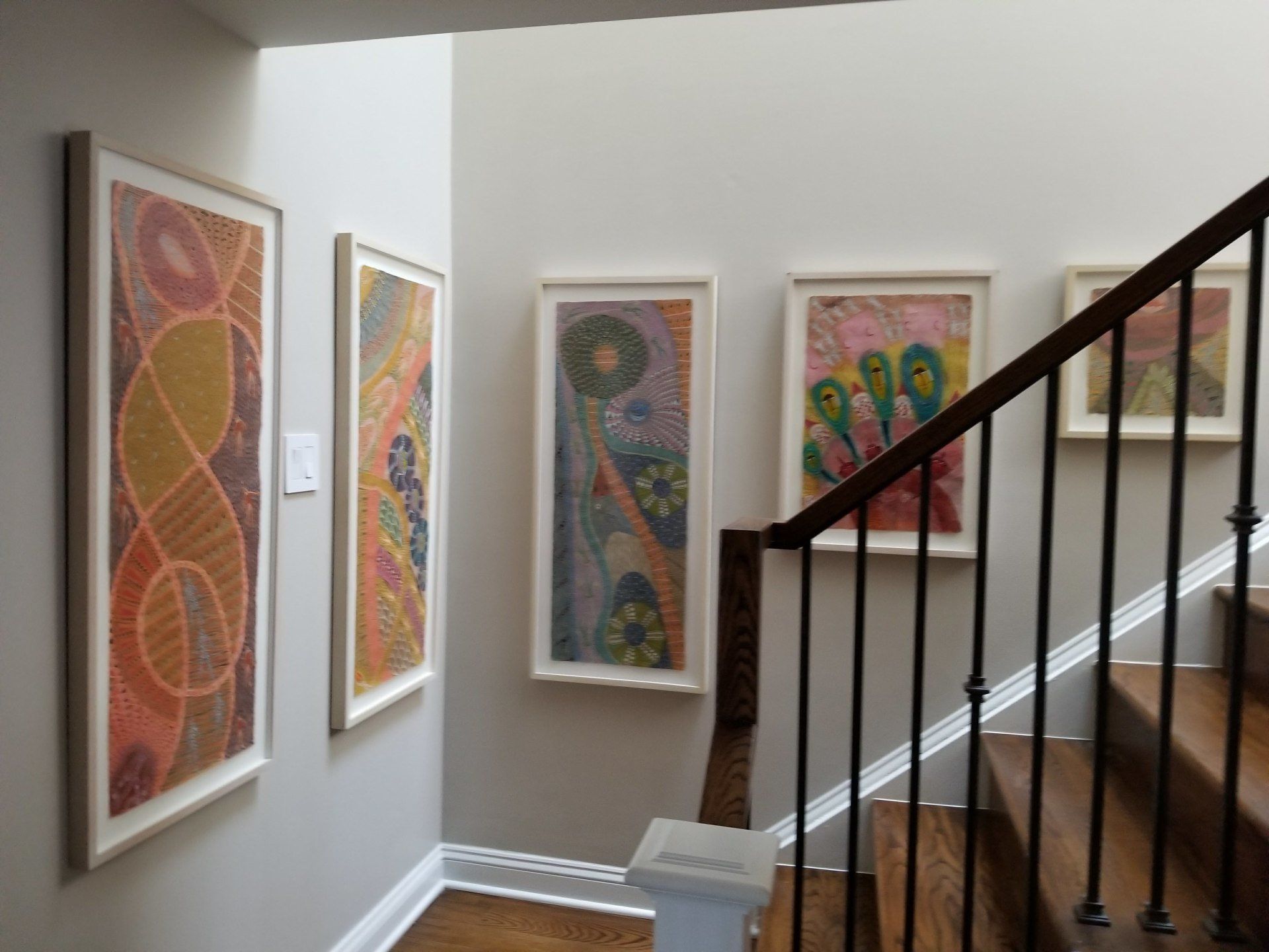 Hallway with artwork on the walls, staircase with railing. Colorful abstract paintings in white frames.