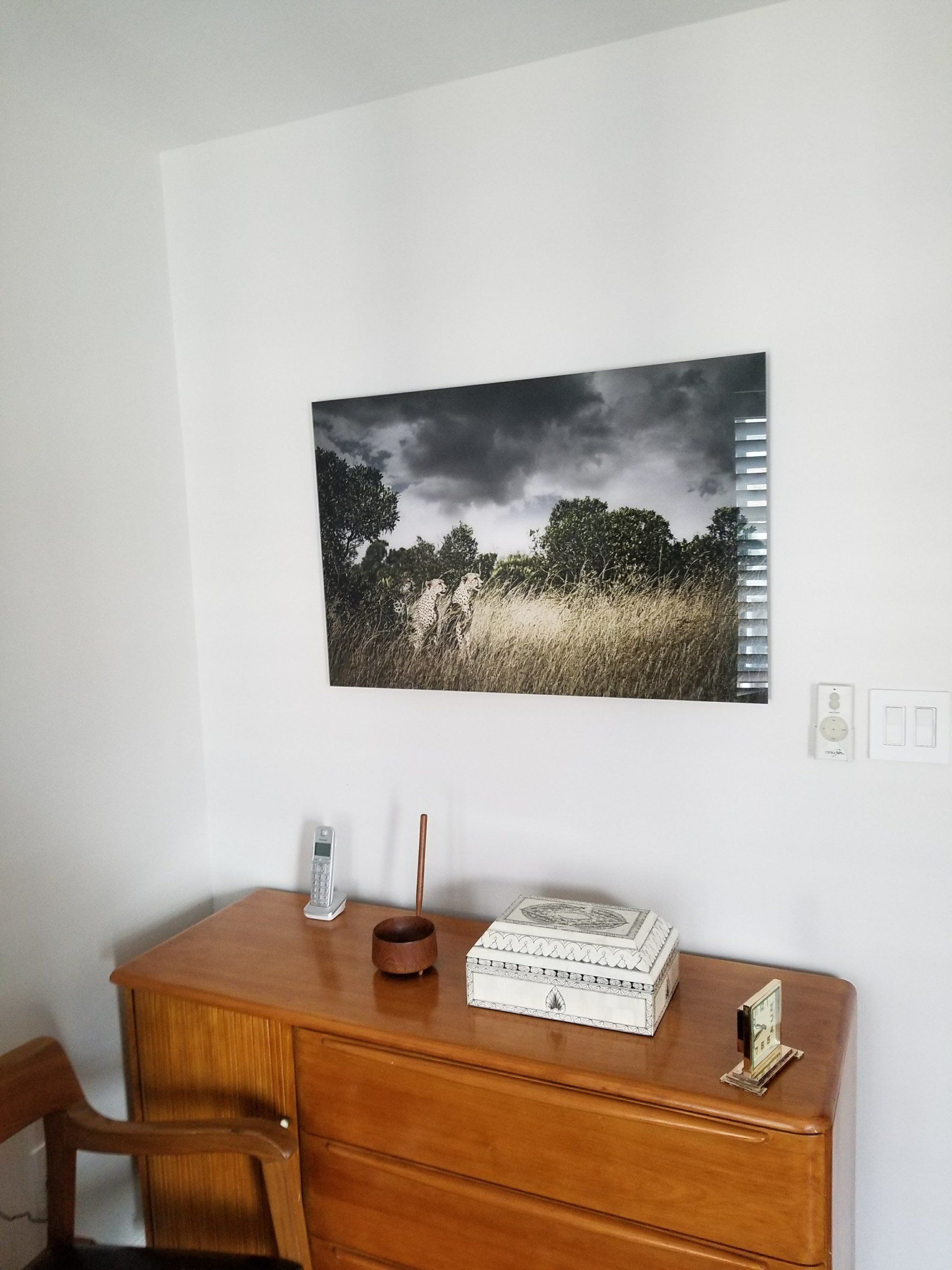 Wooden dresser with decorations beneath a landscape photo on a white wall.
