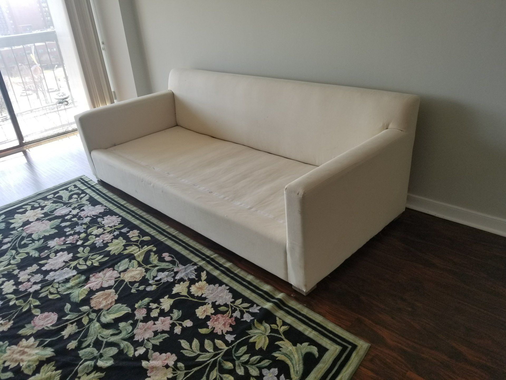 plain white fabric couch with green and black decorative rug by dismantle furniture
