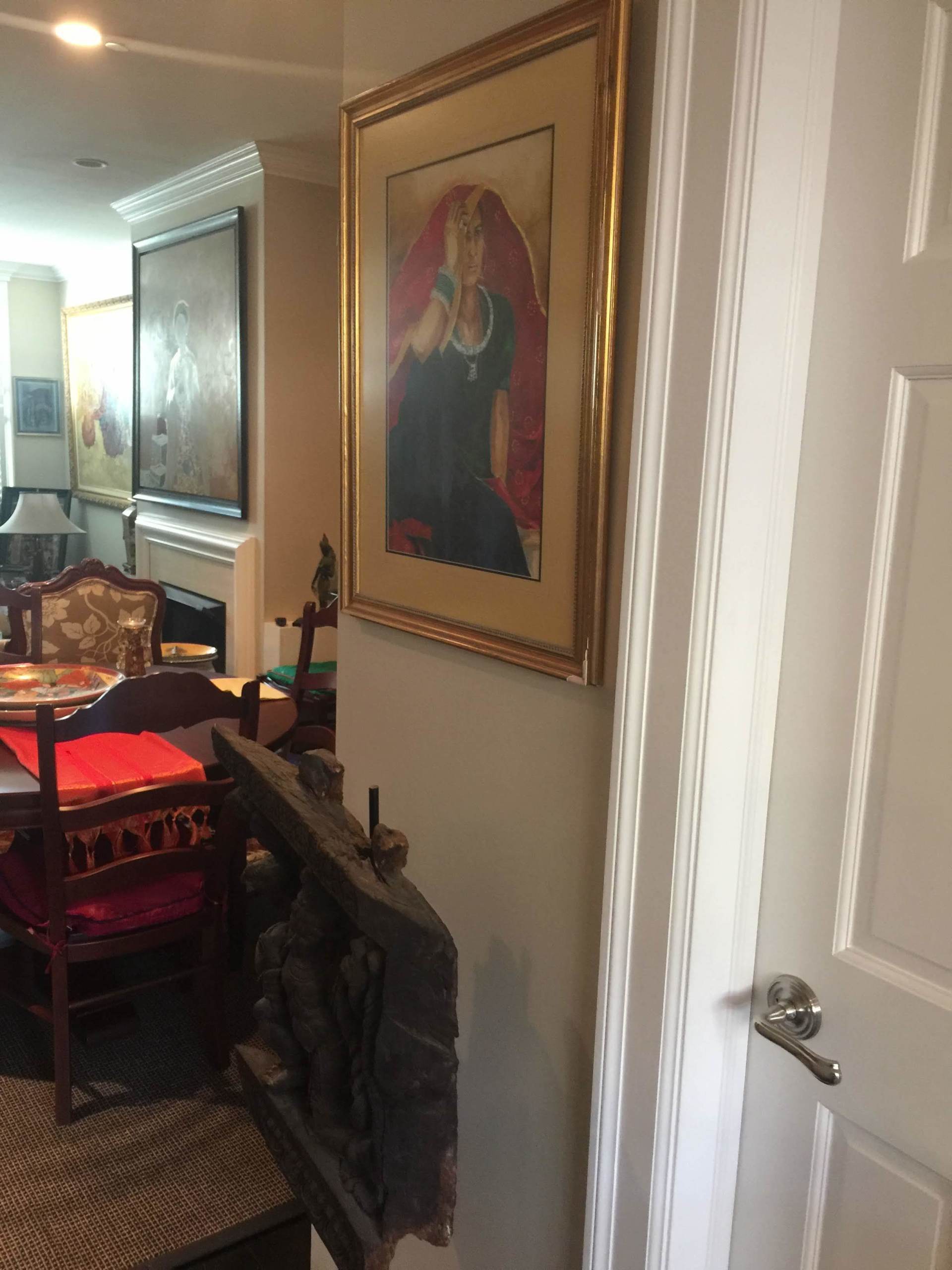 A painting of a woman in a gold frame hangs on a wall next to a door.