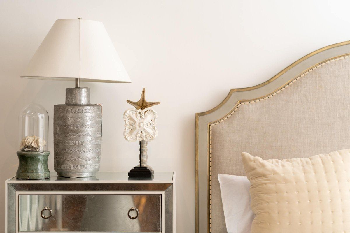 Bedroom nightstand with lamp, decorative objects, and upholstered headboard.
