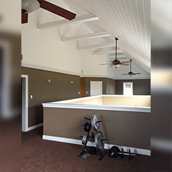A weight rack sits in a carpeted loft room with high, slanted white ceilings and two ceiling fans.
