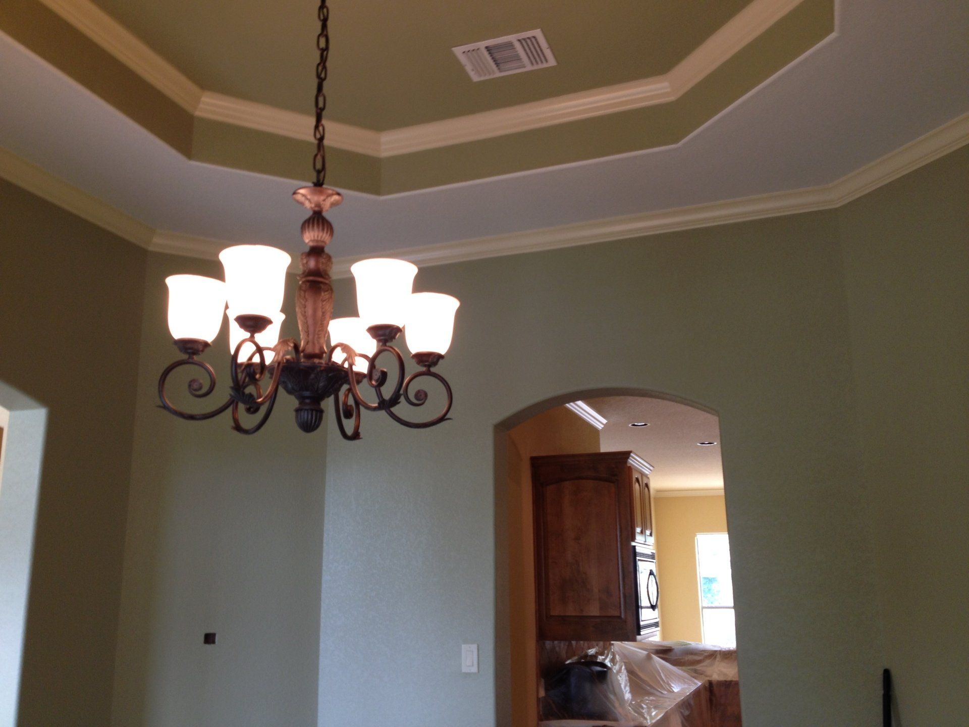 A hanging chandelier with six frosted glass shades suspended from a sage green octagonal tray ceiling above a doorway.
