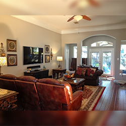 A living room with brown leather seating, a TV, a coffee table, and an arched doorway leading to a sunlit patio.