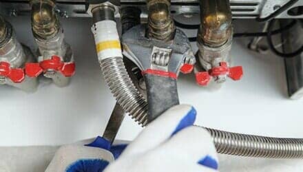 Fixing Pipe Gas Boiler — Willingham Plumbing in VALPARAISO, FL A person using a wrench to tighten a gas line connection near valves, indoors, wearing gloves.
