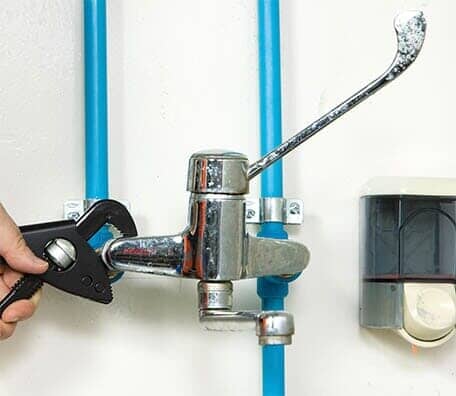 Water Tube — Professional Plumbing Services in VALPARAISO, FL A hand using a wrench to tighten a faucet connected to blue pipes on a white wall.