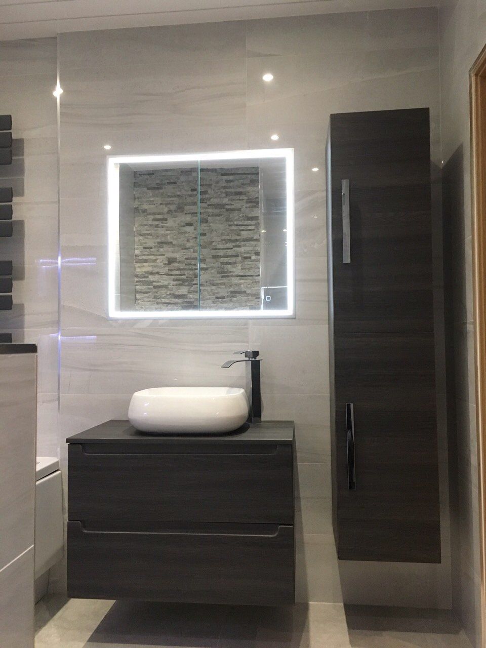 Beautiful bathroom with flushed illuminated mirror cabinet and dark wood countertop vanity unit