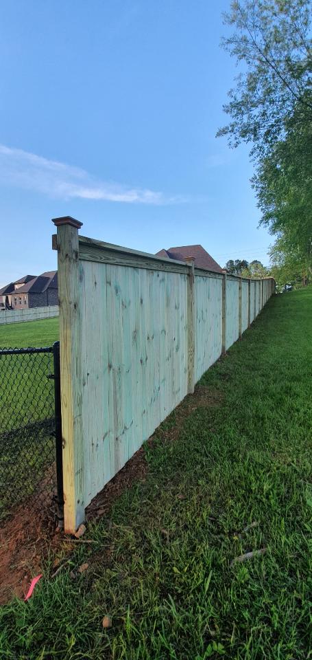A wooden fence is sitting in the middle of a grassy field next to a chain link fence.