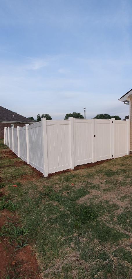 A white fence with a gate in the backyard of a house.