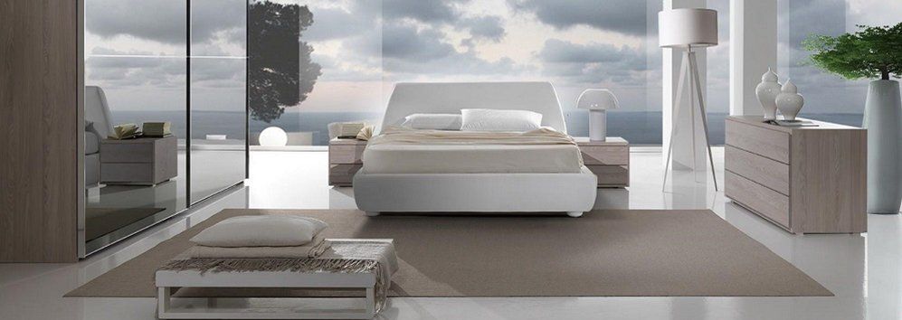 Moderna camera da letto con letto, comodini, cassettiera e lampada da terra, con vista sul mare nuvoloso.