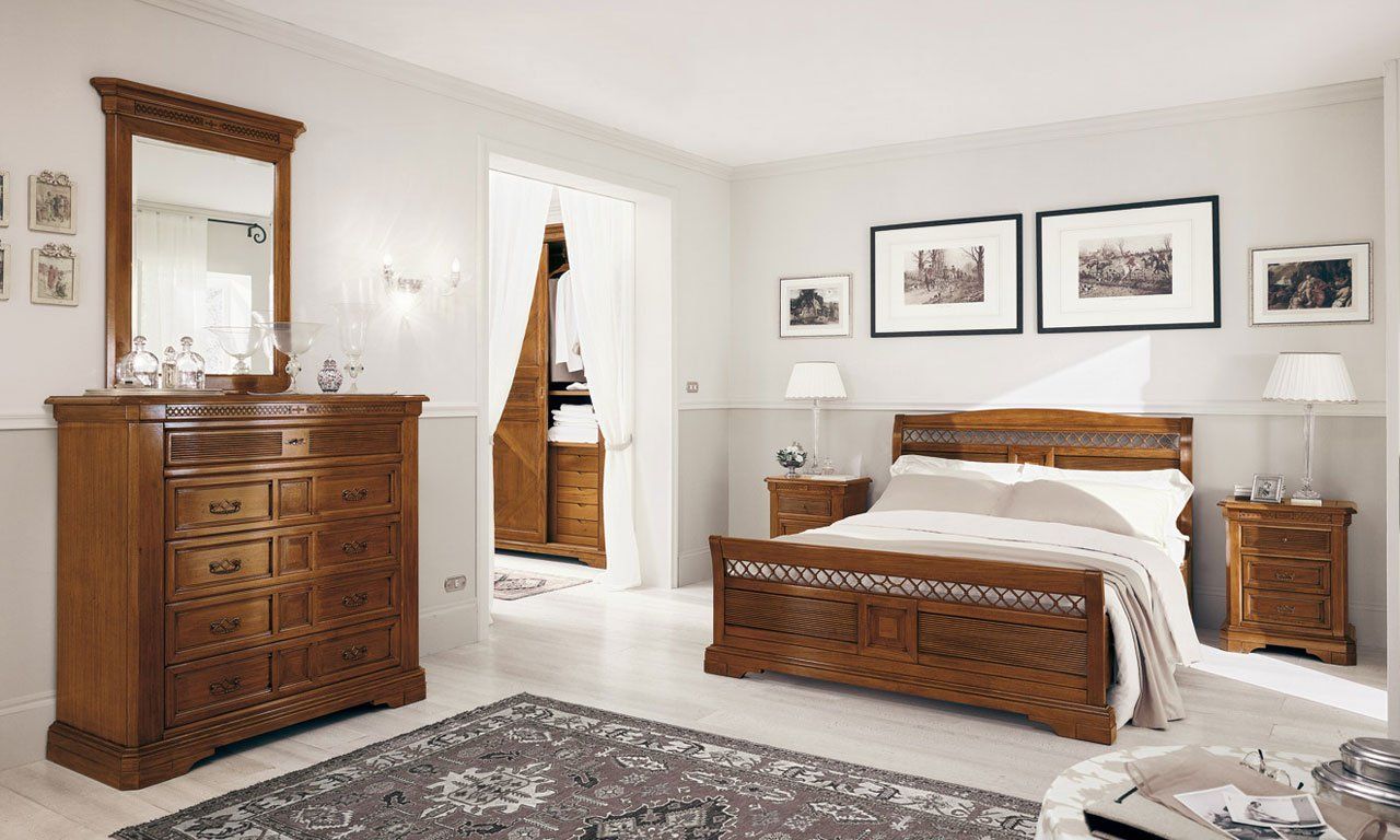 Camera da letto con mobili in legno: letto, cassettiera, specchio, comodini e tappeto. Pareti bianche, opere d'arte decorative.