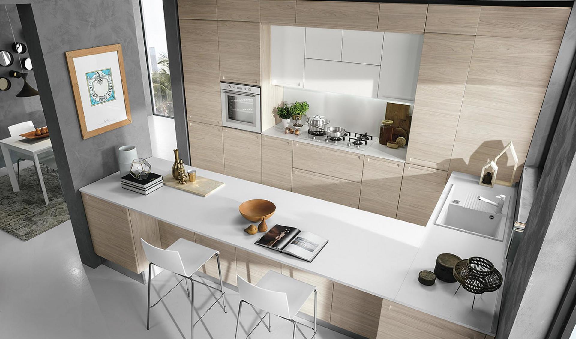 Cucina moderna con mobili in legno chiaro, ripiani bianchi e posti a sedere al bar.
