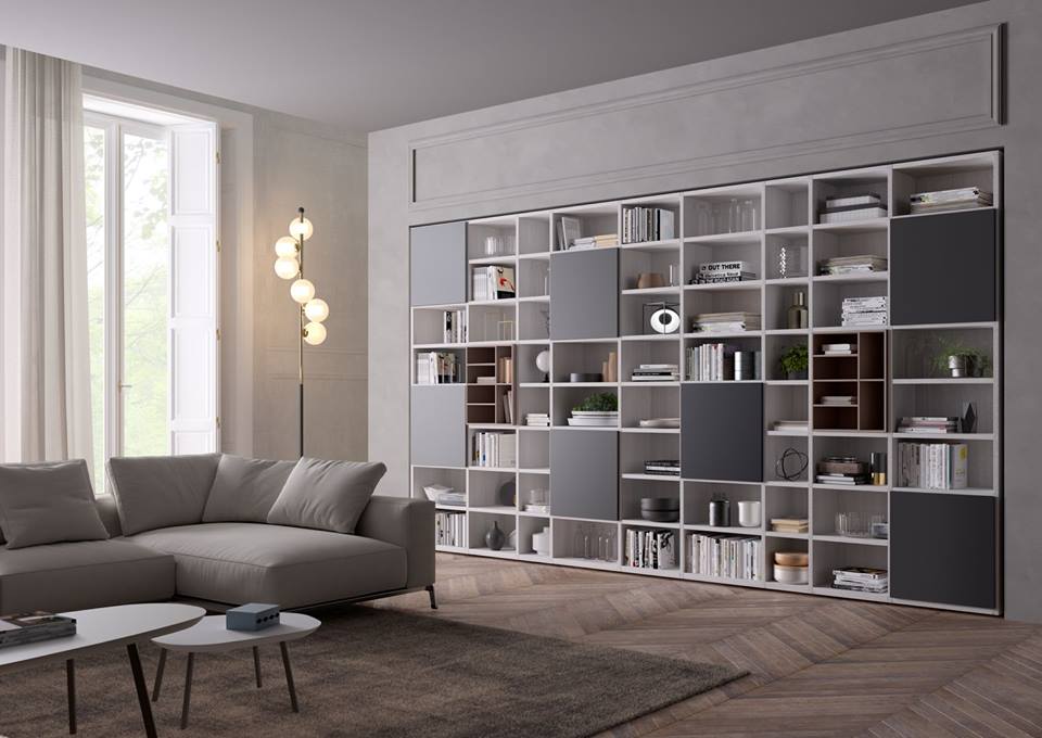 Soggiorno moderno con libreria bianca integrata e pannelli decorativi grigi, con libri, decorazioni e un divano.