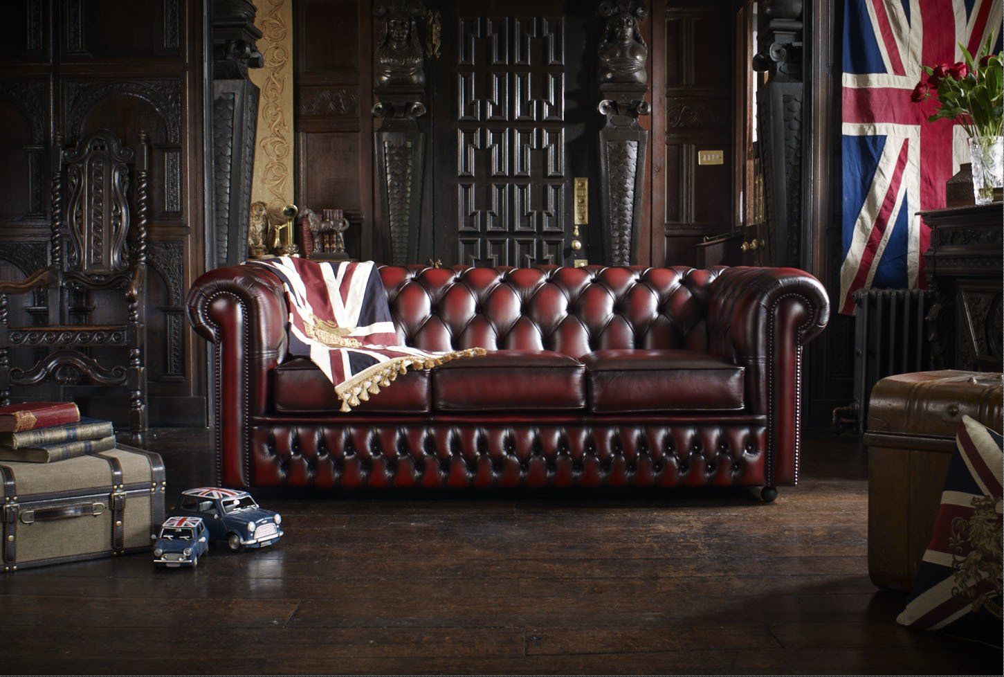 Divano Chesterfield in pelle rossa in una stanza rivestita in legno, con coperta e bandiera Union Jack.
