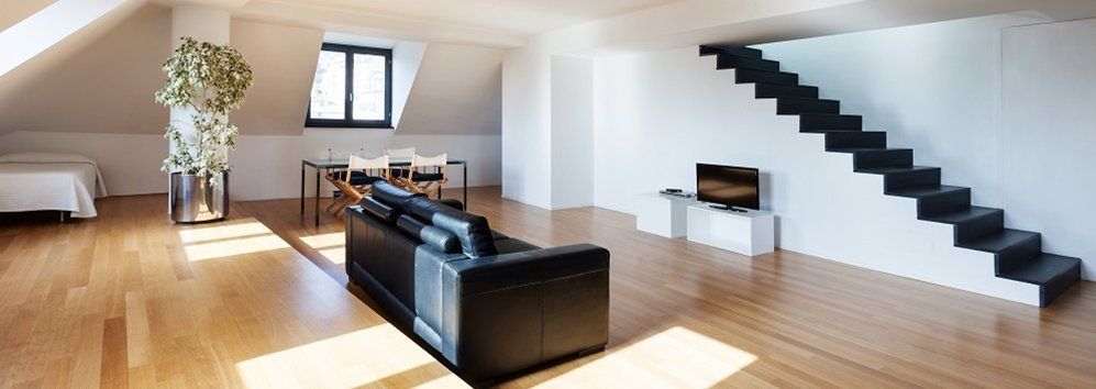 Soggiorno moderno con divano nero, scale e TV. Spazio luminoso con pavimenti in legno.