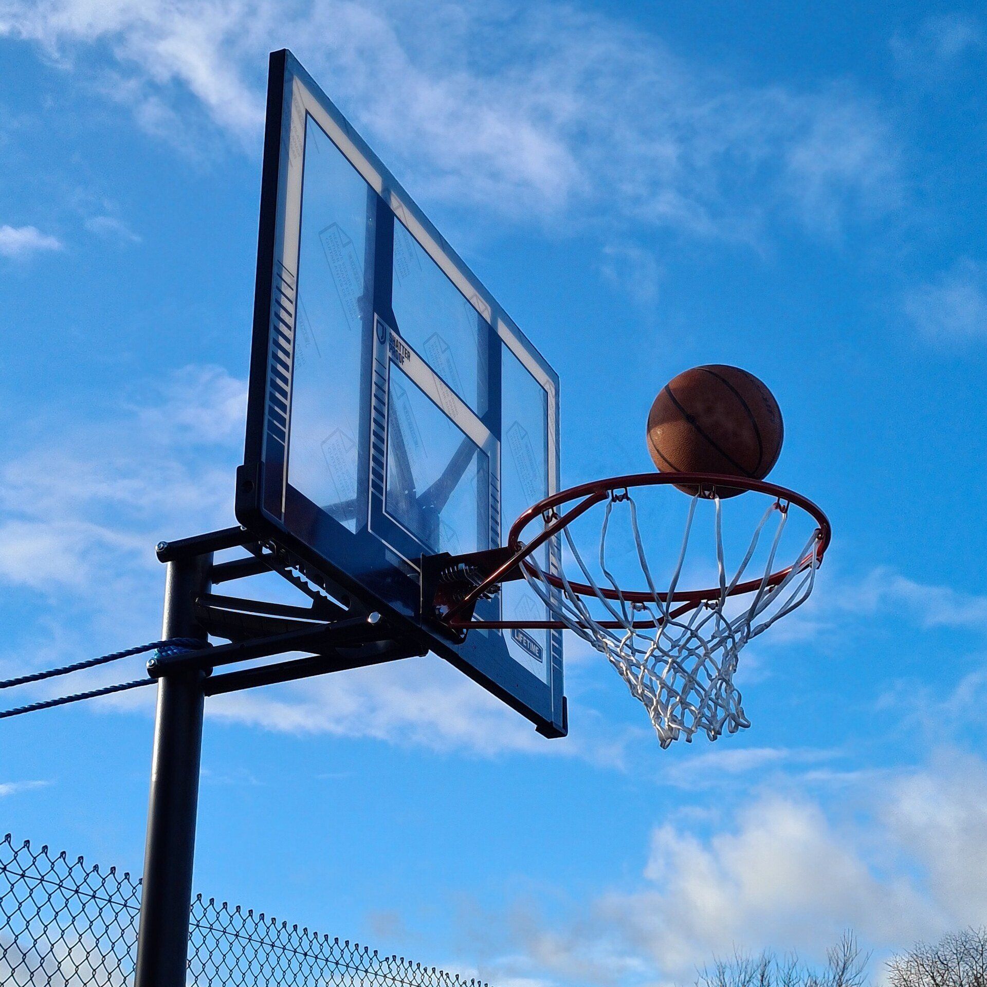 Basketball net with a ball being shot through, on a sunny day