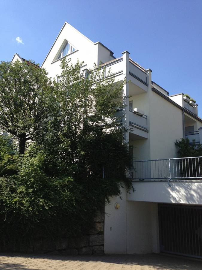 A white building with a balcony and a tree in front of it