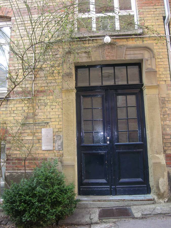 A brick building with a black door and a bush in front of it.