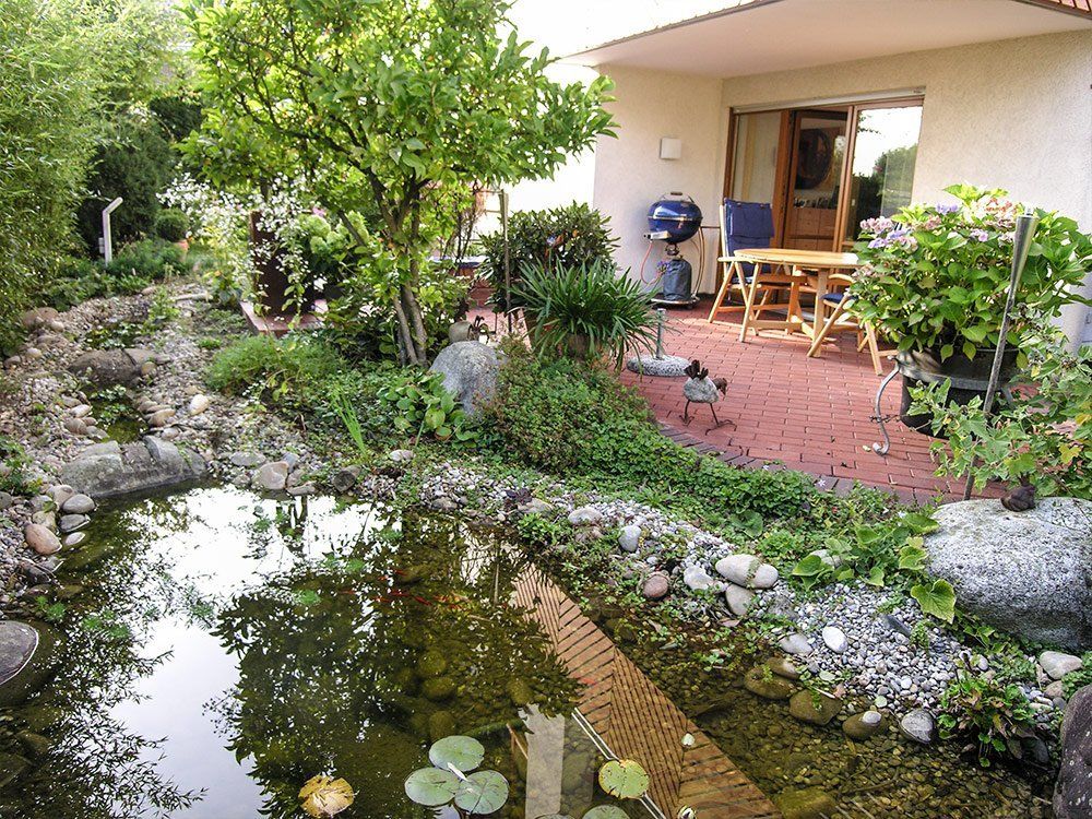 A pond in a garden with a table and chairs in the background