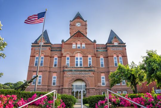 A Couple Speaking to a Lawyer — Omaha, NE — April Cover Attorney At Law Red brick courthouse with a clock tower and American flag. Pink flowers in front.