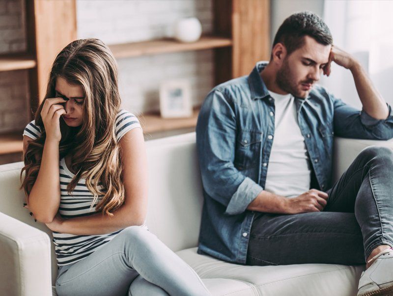 Couple Going Through a Divorce — Omaha, NE — April Cover Attorney At Law Couple sitting on a couch, appearing upset and distant in a living room.
