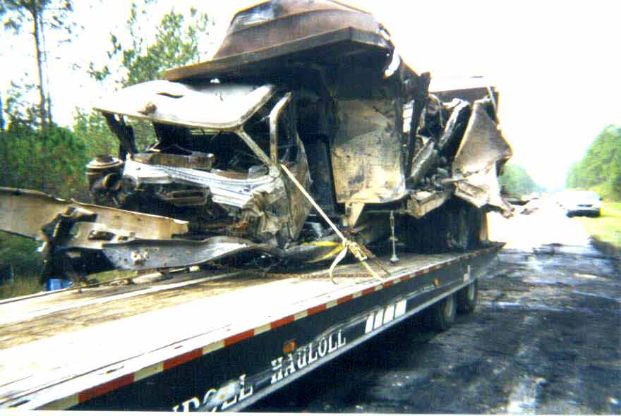 Severely damaged truck on a flatbed trailer, roadside scene.