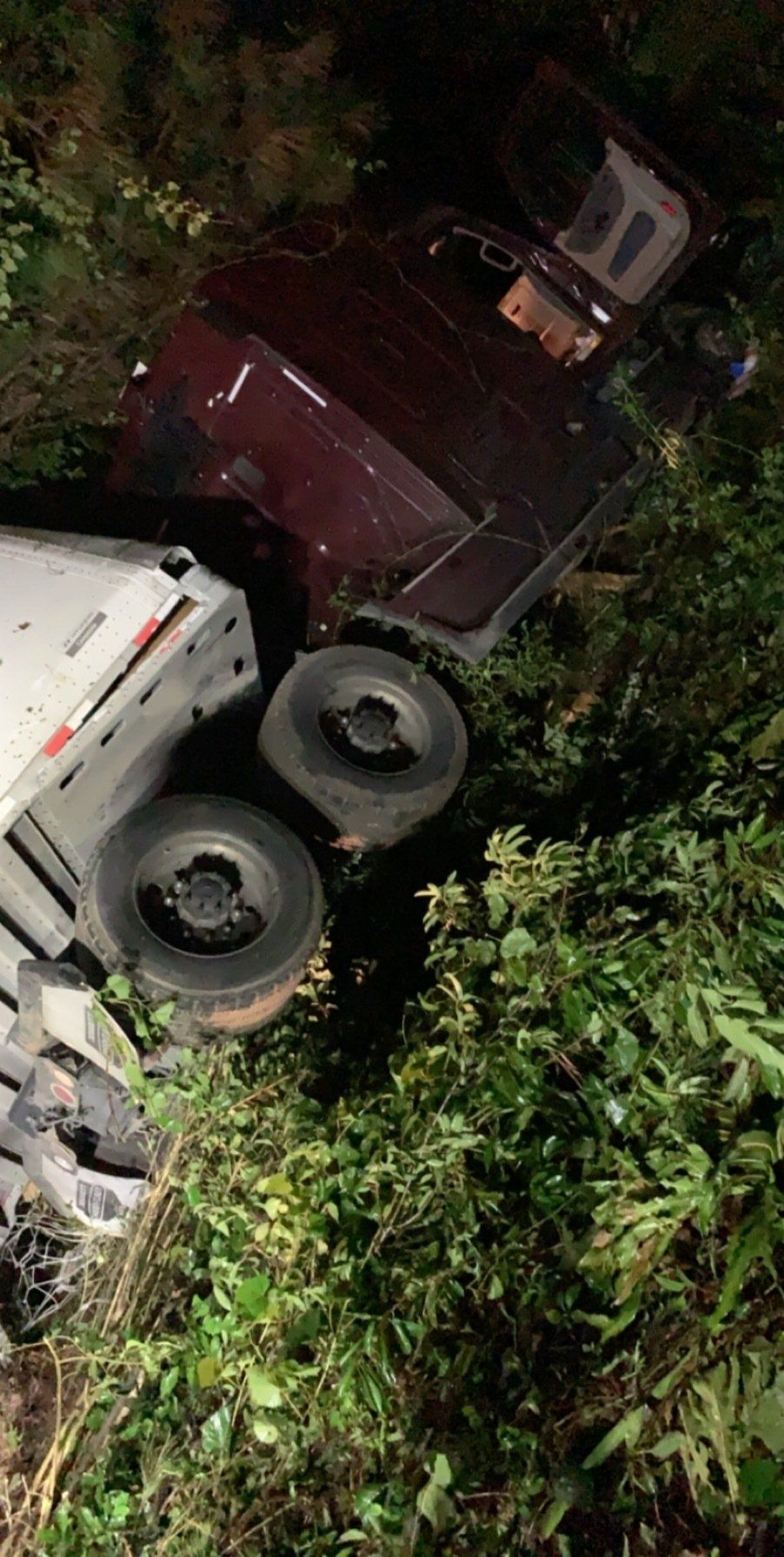 A dark red vehicle overturned in a grassy area with two visible tires.