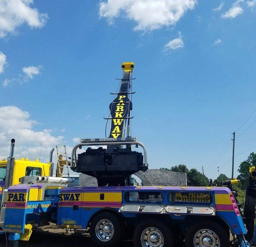 Brightly colored Parkway tow truck against a blue sky, boom extended.