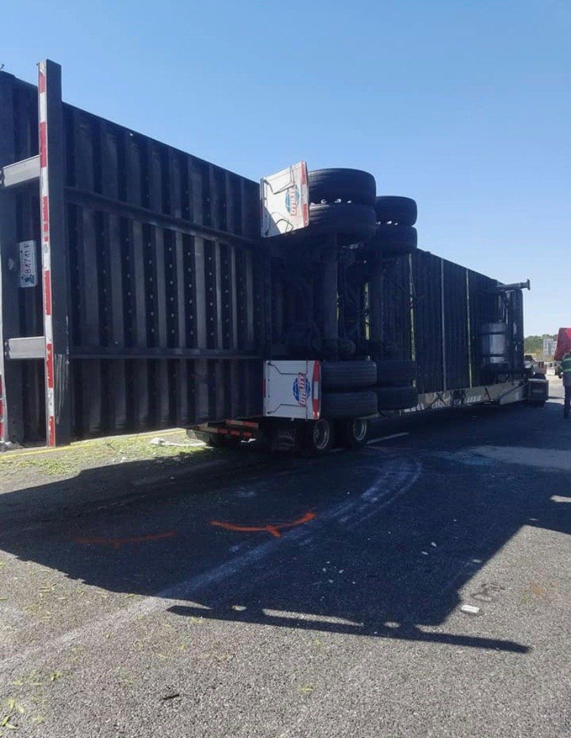 Semi-trailer truck overturned on its side on a paved surface. Black trailer, blue sky.