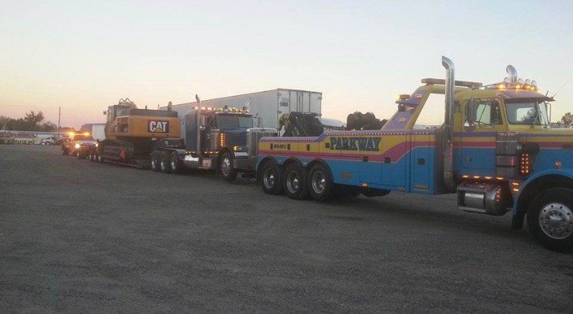 Tow trucks hauling construction equipment and a trailer on a lot.