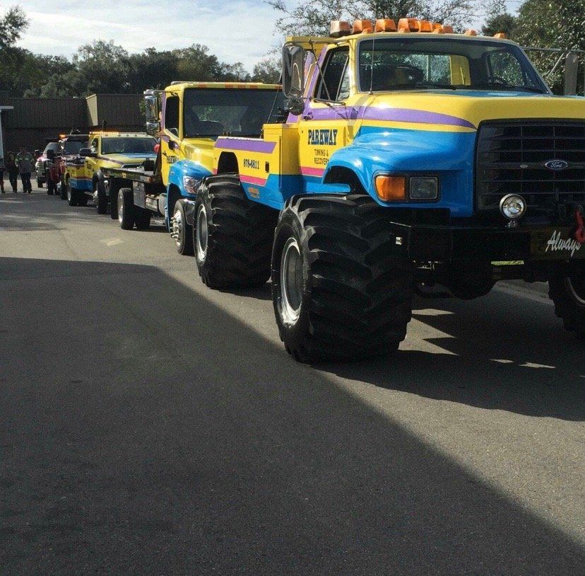 Line of colorful tow trucks on a road, each with oversized tires.