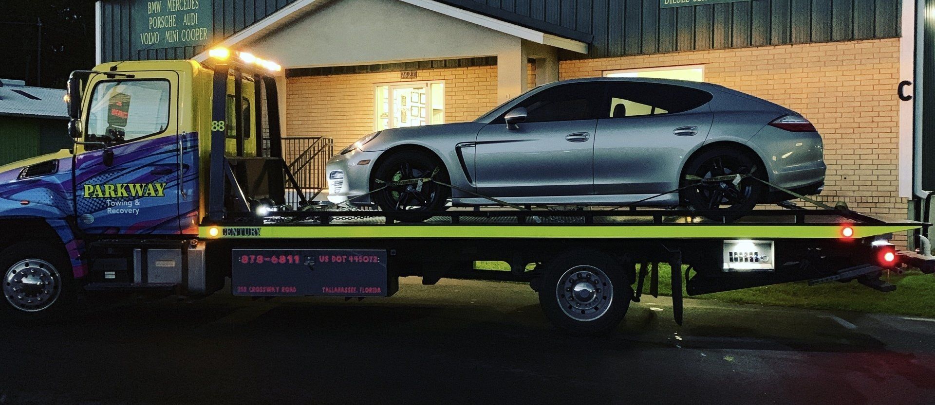 A silver Porsche sedan is loaded on a flatbed tow truck at night.