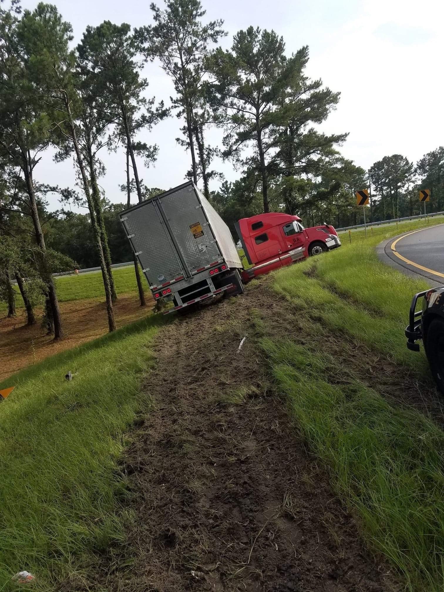UPS semi-truck tilted on grassy embankment near a curve in the road. Red cab, tan trailer.