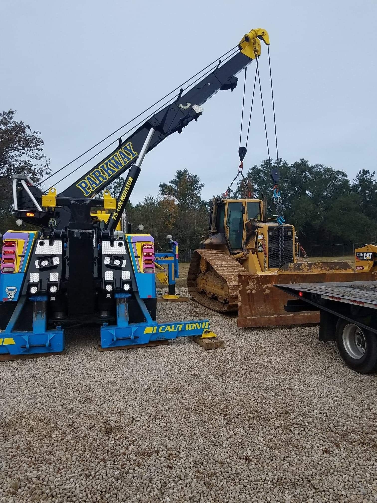 Tow truck lifting a yellow bulldozer onto a flatbed trailer.