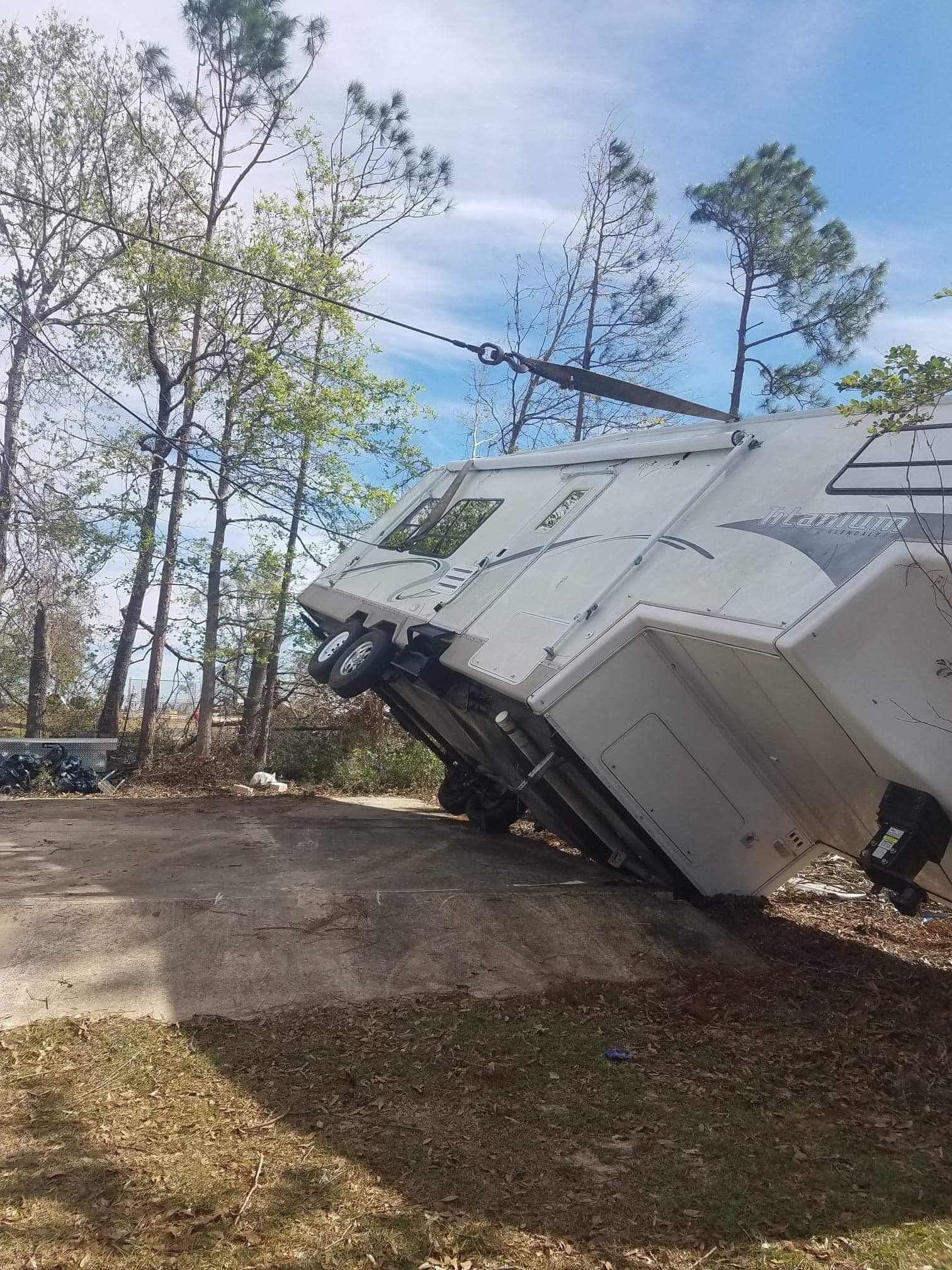 A white recreational vehicle is tilted on a dirt surface being towed by a cable.