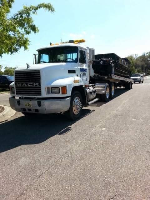 White Mack truck with a trailer carrying cargo parked on a paved road on a sunny day.