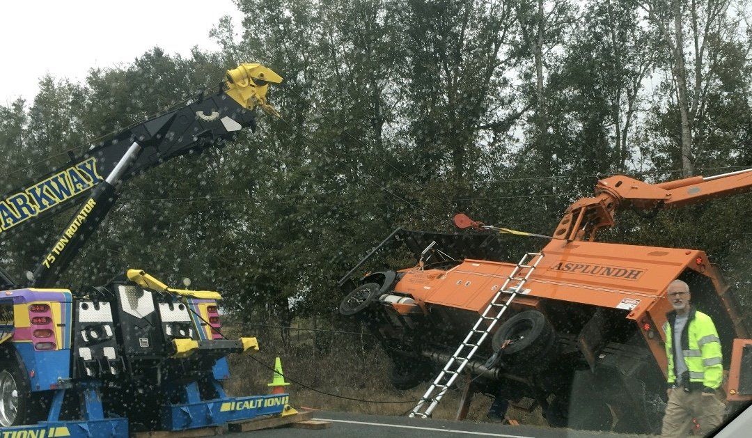 Orange truck overturned on side of road being lifted by tow truck.