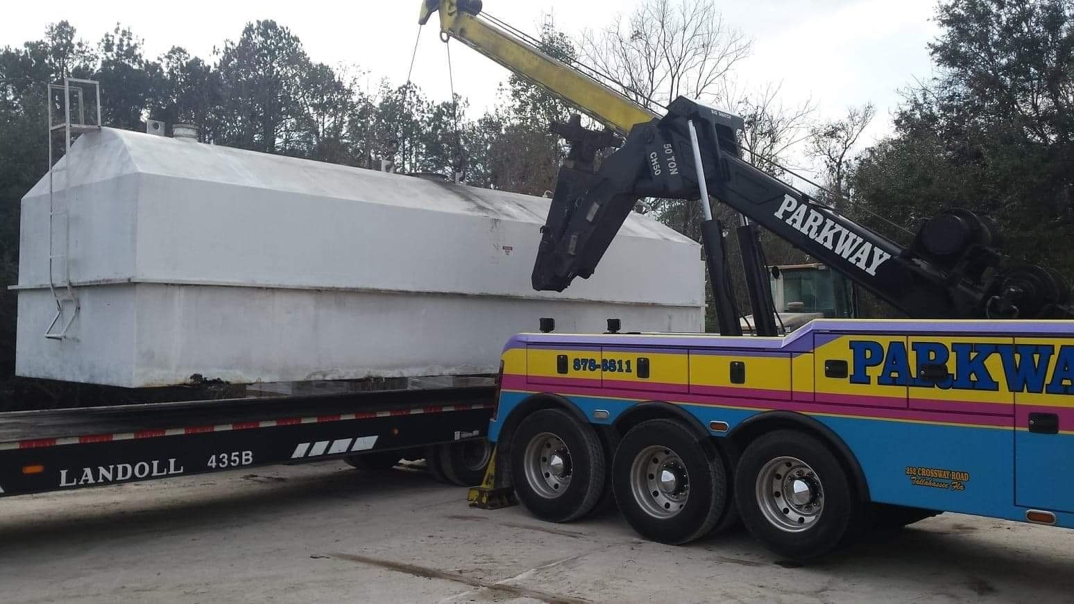 Tow truck lifting a large white object onto a flatbed trailer, 