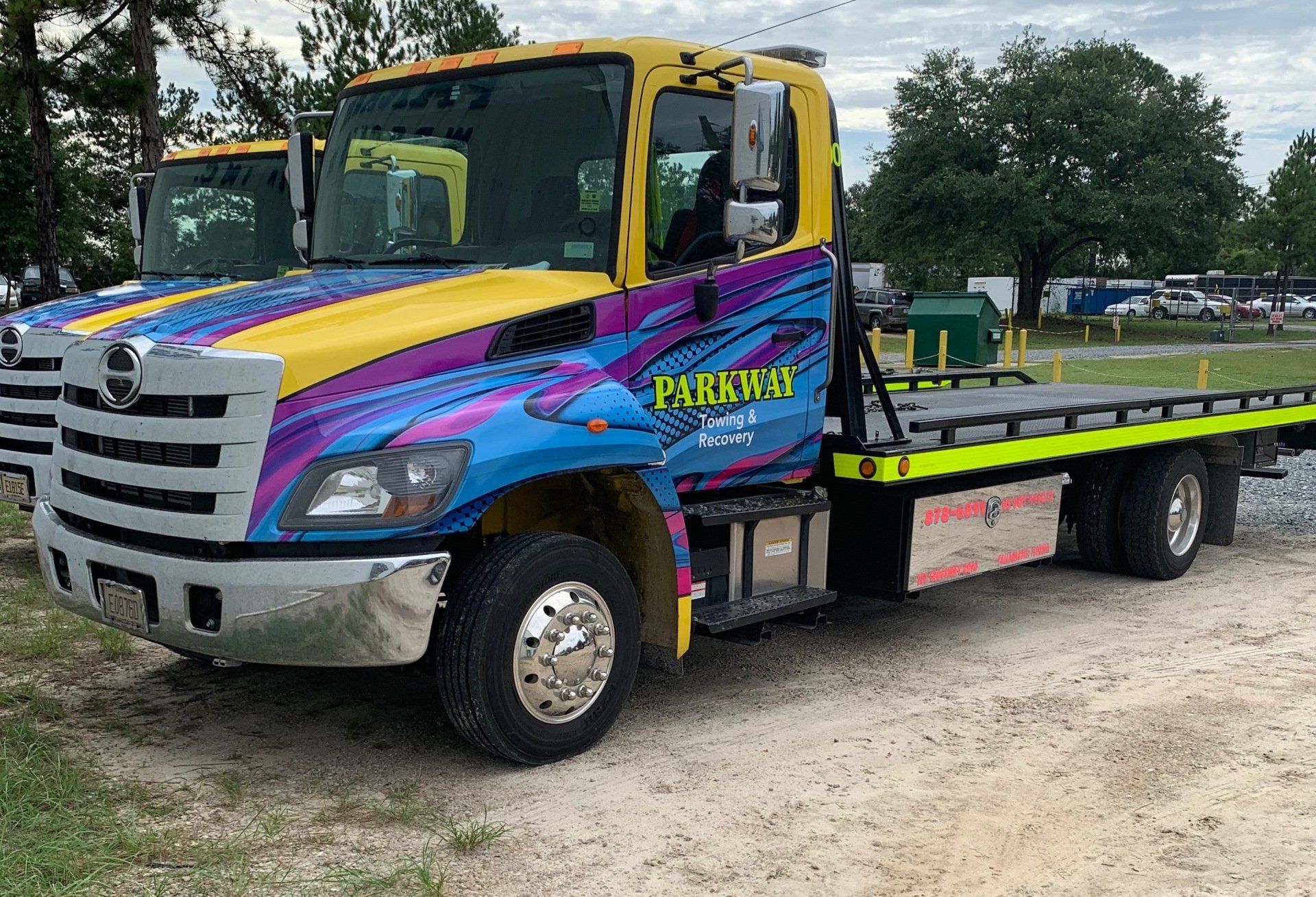 Yellow and blue Parkway Towing flatbed truck on gravel.