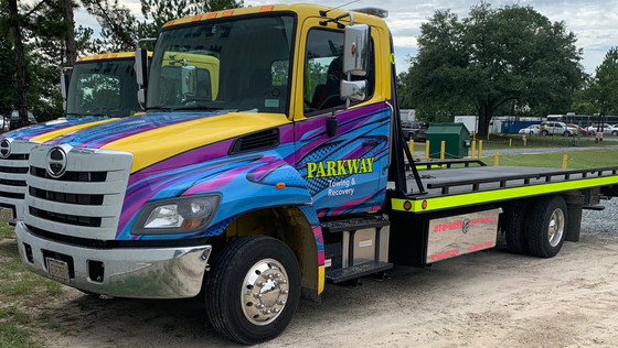 Yellow, blue, and purple tow truck parked on gravel. 